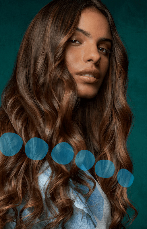 Woman with long, wavy brown hair looks slightly to the side against a teal background, highlighting her expert hair cut and style. Blue translucent circles are overlaid across the lower part of the image. - Pure Salon Spa, KY